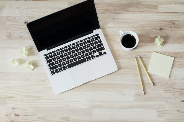 photo of an open laptop, crumpled paper, notepad, pencils and cup of coffee