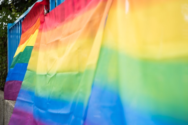 photo of rainbow flags attached to a blue fence blowing in the wind