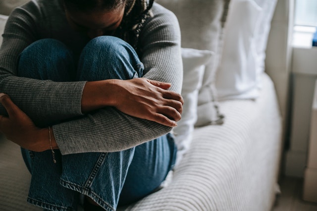 A woman sitting on a bed, curled in a ball wrapping her arms around her knees