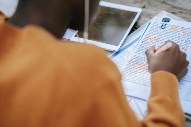 Close up photo looking over a person's shoulder as they read an article and hold a pen