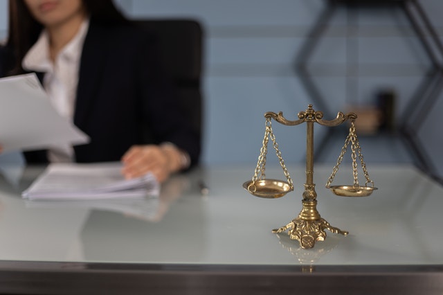 A person sitting behind a desk with papers on the desk and scales sitting on the corner of the desk