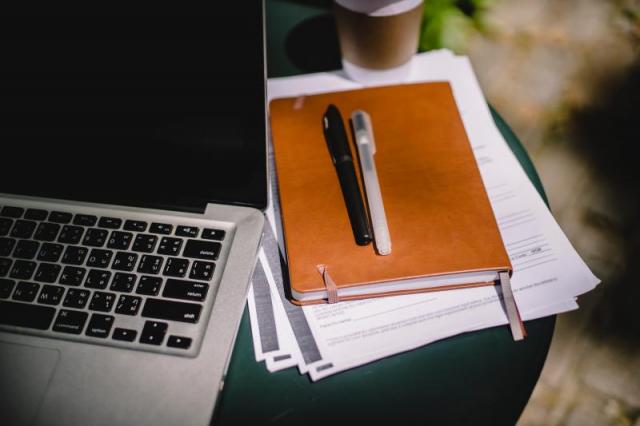 a laptop with files and a pen next to it