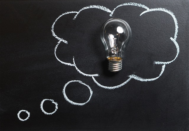 photo of a blackboard with chalk drawn thought bubbles with a lightbulb in the biggest bubble