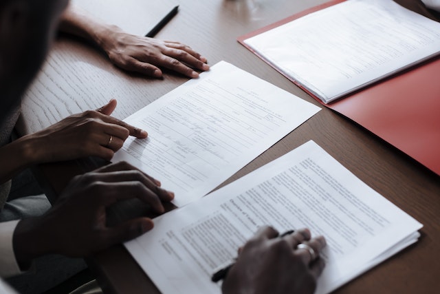 close up photo of 2 people's hands reading and signing paperwork