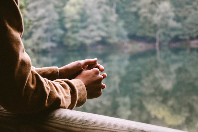 close up photograph of a person leaning on a railing holding their hands